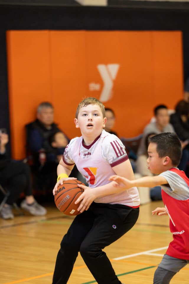 两个穿着基督教青年会篮球服的小男孩正在打篮球。其中一个男孩正准备投篮，而另一个男孩则在盖帽。